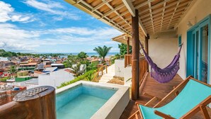 A rooftop pool area with a hammock and lounge chairs, overlooking a coastal town.