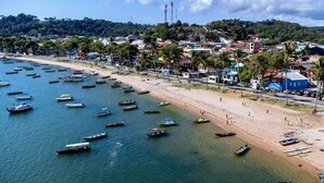 A coastal town with a beach lined with boats and a densely built residential area with palm trees.