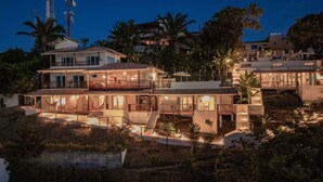 A multi-story house with a large balcony, outdoor seating, and a swimming pool.