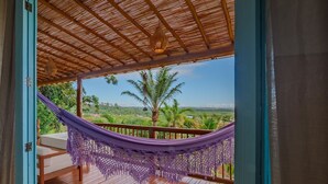 A wooden deck with a purple hammock and a view of a green landscape.