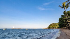 A beach with clear skies, calm waters, a lighthouse, and palm trees.