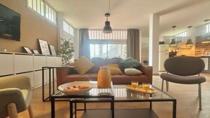 Una sala moderna con una mesa de centro de vidrio, un sofá y un comedor con una cocina al fondo.