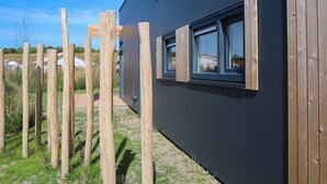 A modern building with a dark exterior, wooden window frames, and a wooden fence in the foreground. - Modern Retreat Near Beach ('s-Gravenzande)