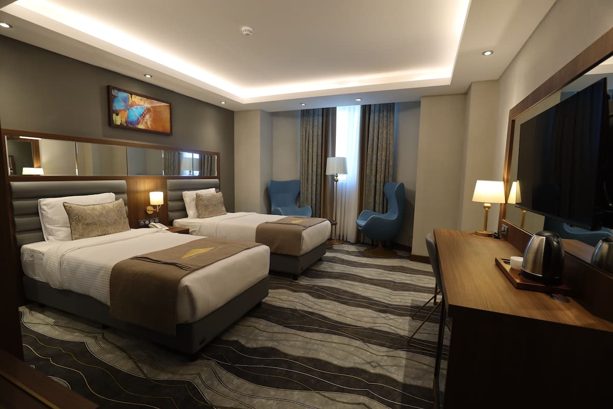 A hotel room with two beds, a desk, a chair, a TV, and a large mirror.