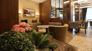 Een hotellobby met een ronde tafel, comfortabele zitplaatsen, een decoratieve plant en een schilderij aan de muur.