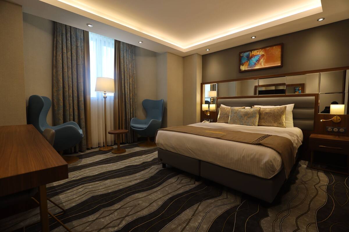 A hotel room with a large bed, two armchairs, a small table, and a desk.