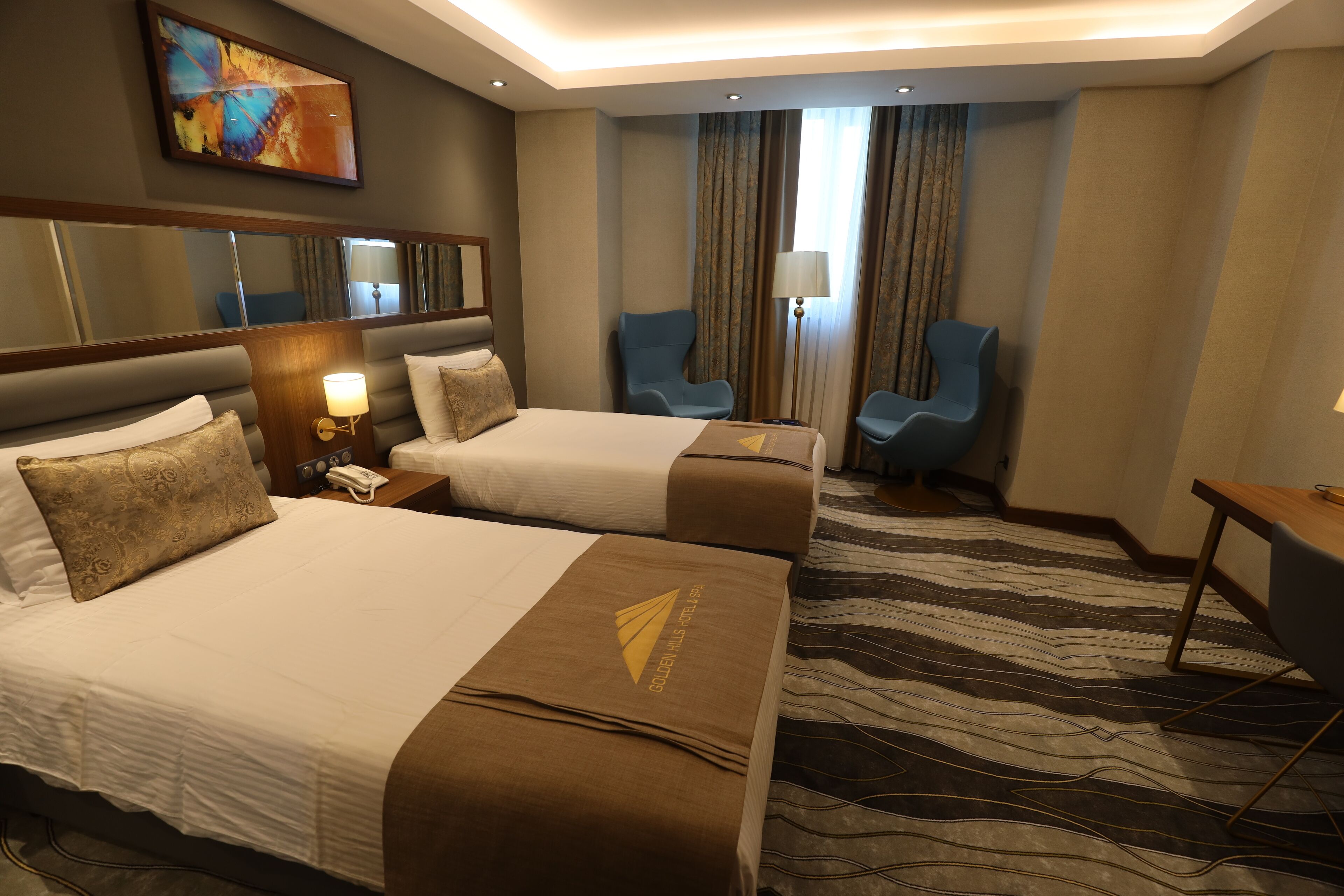 A hotel room with two beds, a desk, a chair, a lamp, and a large mirror.