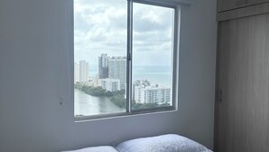 A bedroom with a bed, a window with a view of buildings and a river, and a wardrobe.