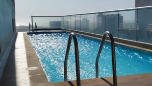 A rooftop pool with metal railings and a clear view of the city skyline in the background.