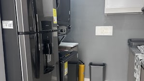 A compact kitchen with a refrigerator, a microwave, a small sink, and a trash bin.