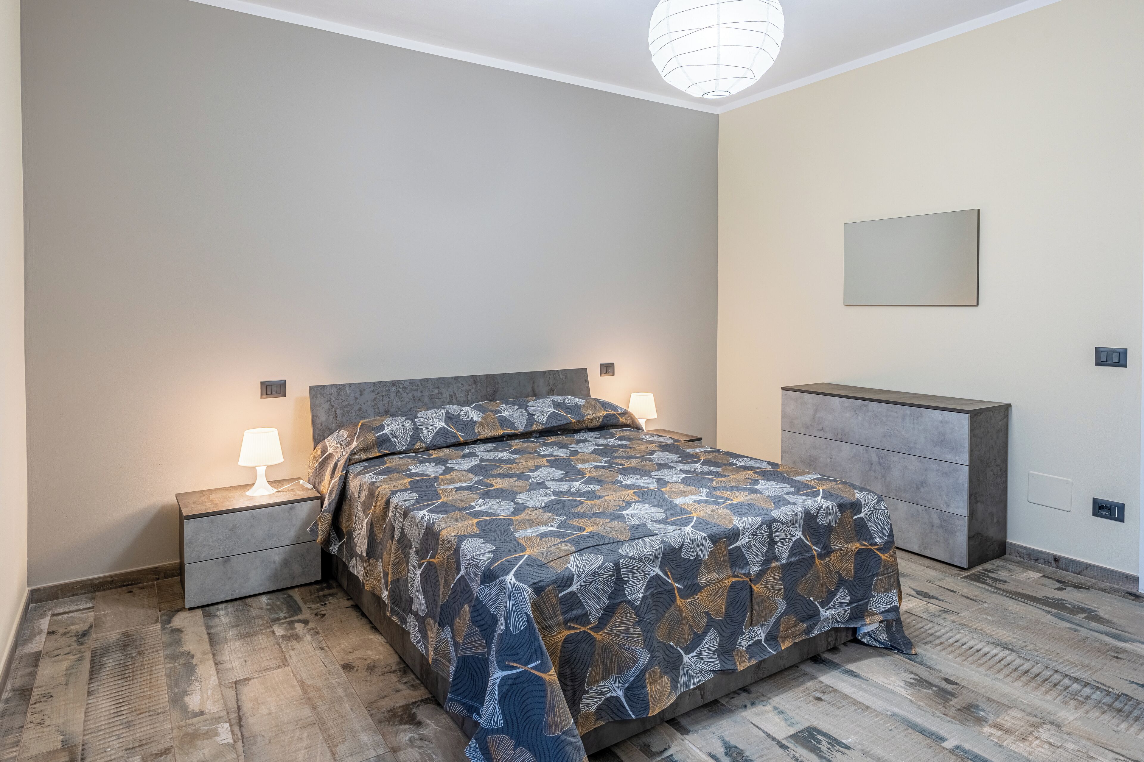 A bedroom with a bed, nightstands, a dresser, and a wall-mounted mirror.