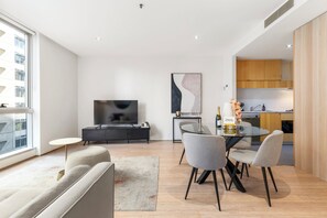 A modern living room with a sofa, a dining table with chairs, a TV, and a kitchen area with wooden cabinets.