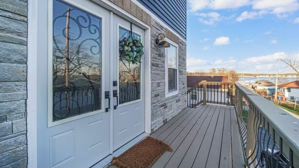 Una casa con fachada de piedra, terraza de madera y puerta blanca con panel de vidrio.