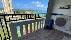 Un balcón con vista a la playa, un cartel que dice "BEACH" y un equipo de aire acondicionado.