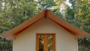 A small, single-story cabin with a pitched roof, a wooden deck, and two wooden chairs outside. - Field Trip Unit 5 XL Canvas Cabin Family & Dog-Friendly (Travelers Rest)