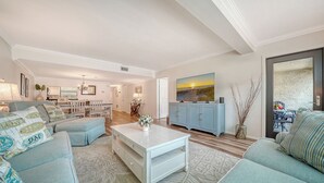 A spacious living room with a dining area, a television, and a view of the outdoors. - Paradise Awaits: Condo with an ocean view steps from Siesta Key Beach! (Sarasota)