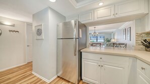 A modern kitchen with white cabinetry, a stainless steel refrigerator, and a wooden floor. - Paradise Awaits: Condo with an ocean view steps from Siesta Key Beach! (Sarasota)