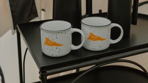 A table with two white mugs with orange flags, a black coffee pot, and a French press. - Field Trip Unit 8 Small Bell Tent (Travelers Rest)