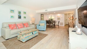 A living room with a sofa, armchairs, a coffee table, and a dining area with a table and chairs. - Lovely, beachfront condo. Steps to Siesta Key #1 Beach in America. (Sarasota)