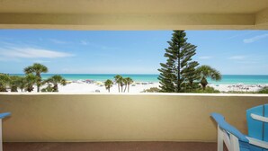 A balcony with a view of a beach, palm trees, and a clear sky.