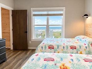 Un dormitorio con cama, cómoda, ventana con vista al océano y puerta.