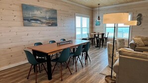 A room with a wooden floor, a dining table with chairs, a sofa, and a lamp. - Stunning Oceanfront Retreat w/ Private Pool, Elevator, Handicap Accessibility (Ocean Isle Beach)