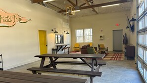 Ein geräumiger Innenbereich mit Picknicktischen, einer gelben Tür und einer Sitzecke mit Stühlen und einer Couch.
