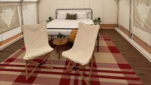 Ein Zelt mit einem Bett, zwei Stühlen und einem kleinen Tisch.
