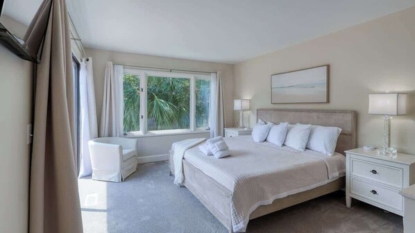 A bedroom with a large bed, bedside tables, a window with curtains, and a painting on the wall.