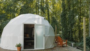 A dome-shaped tent with an open door, a wooden deck, a chair, and a potted plant. - Field Trip Unit 16 GeoDome (Travelers Rest)