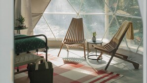 A cozy, well-lit room with a large window, a bed, a chair, a table, and a bag on the floor. - Field Trip Unit 16 GeoDome (Travelers Rest)