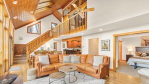 Un vaste espace de vie comprenant un grand canapé en cuir, un ventilateur de plafond en bois et un escalier menant à un niveau supérieur.