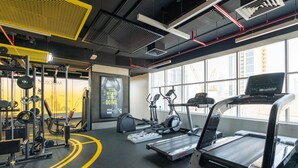 A modern gym with cardio equipment, weight machines, and a large window offering a view of the city. - Burj Khalifa DownTown Hostell (Dubai)