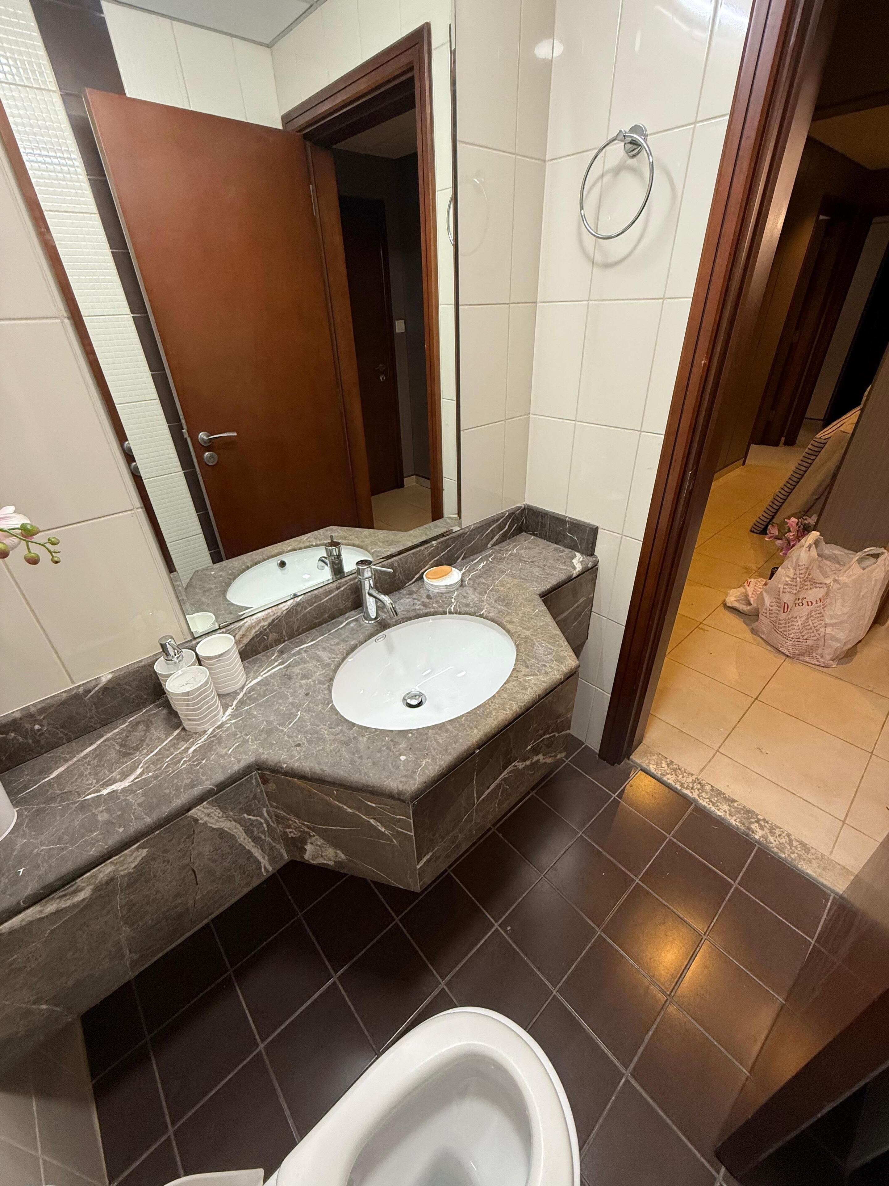 Un baño con lavamanos de mármol, dos espejos, un inodoro y zona de ducha.