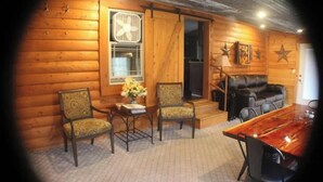 A cozy log cabin interior with a dining table, two chairs, a sofa, and a fireplace.