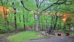 A forested campsite with a gravel path, picnic table, and fire pit.