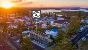 An aerial view of a residential area with houses, a large building with a blue roof, and a body of water in the background. - Seaspray 6 - Short walk to the beach and Yamba's CBD (Yamba)
