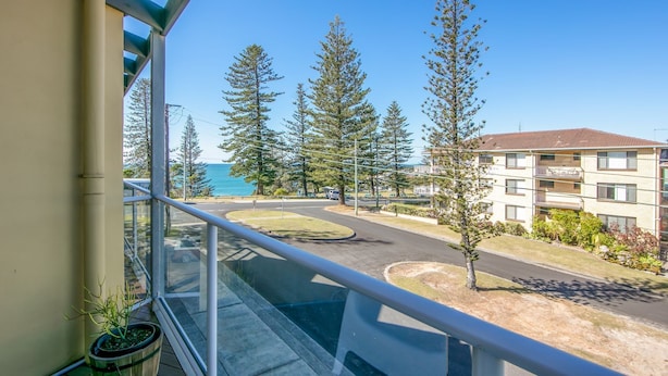 A balcony with a view of a road, trees, and a building with a sign that reads "PARKING". - Seaspray 6 - Short walk to the beach and Yamba's CBD (Yamba)