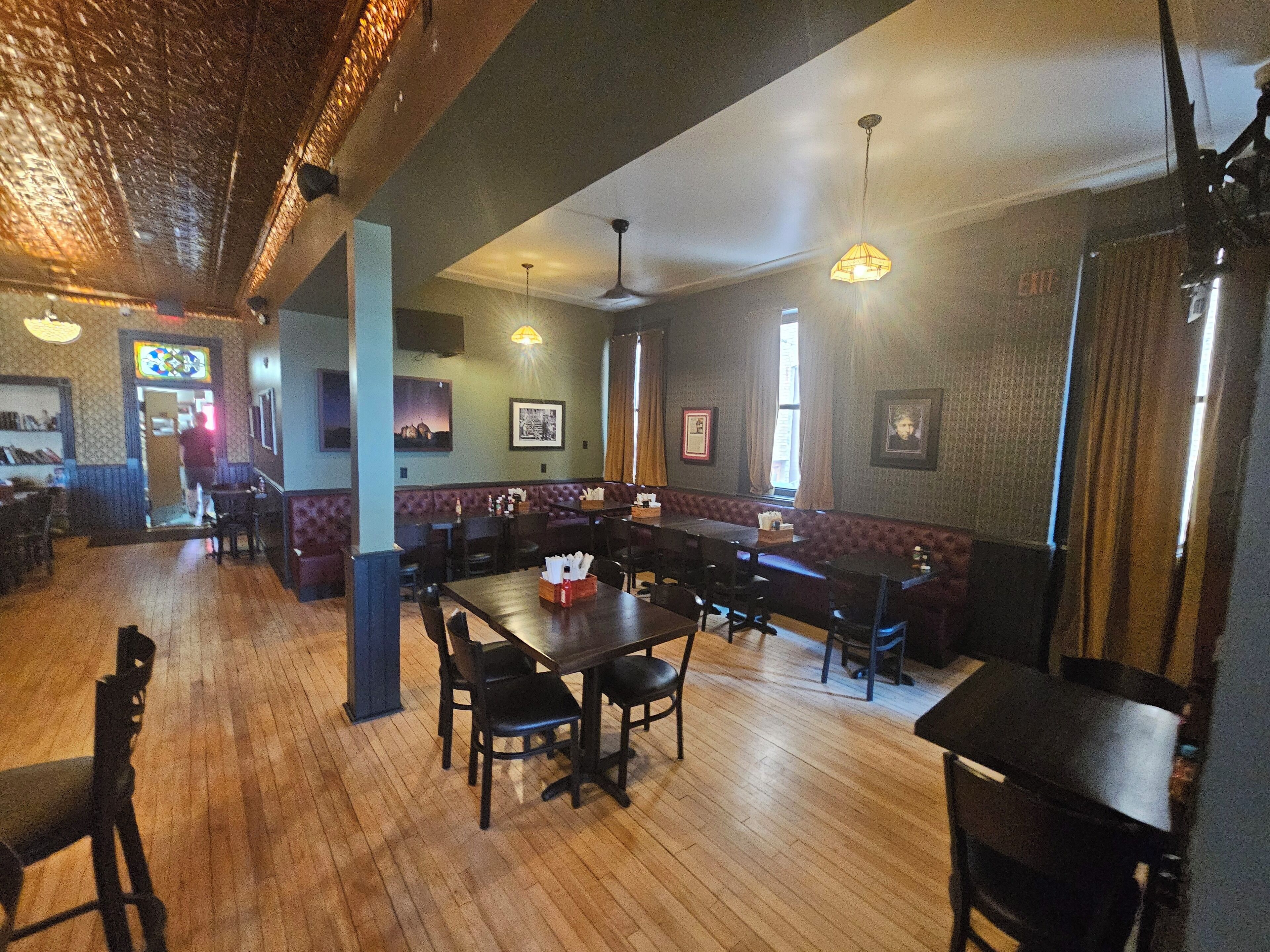A restaurant with wooden floors, booths, and tables. There are framed pictures on the walls and a stained glass window.