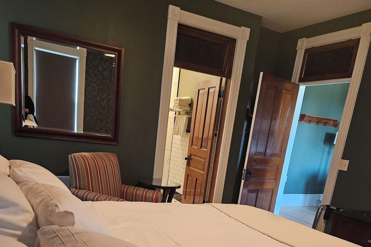 Una cama bien hecha con sábanas blancas, una silla a rayas y una mesita.