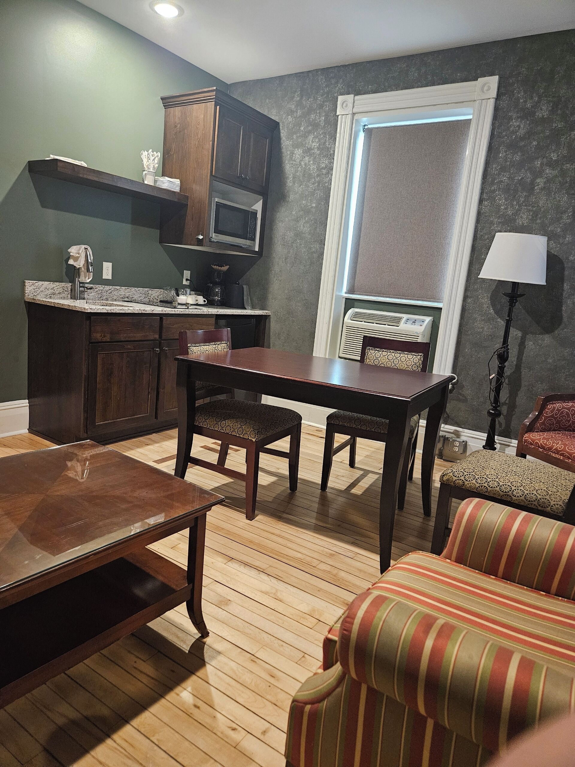 Um espaço compacto para viver, com mesa e cadeiras de jantar, sofá e área de cozinha, incluindo micro-ondas e armários.