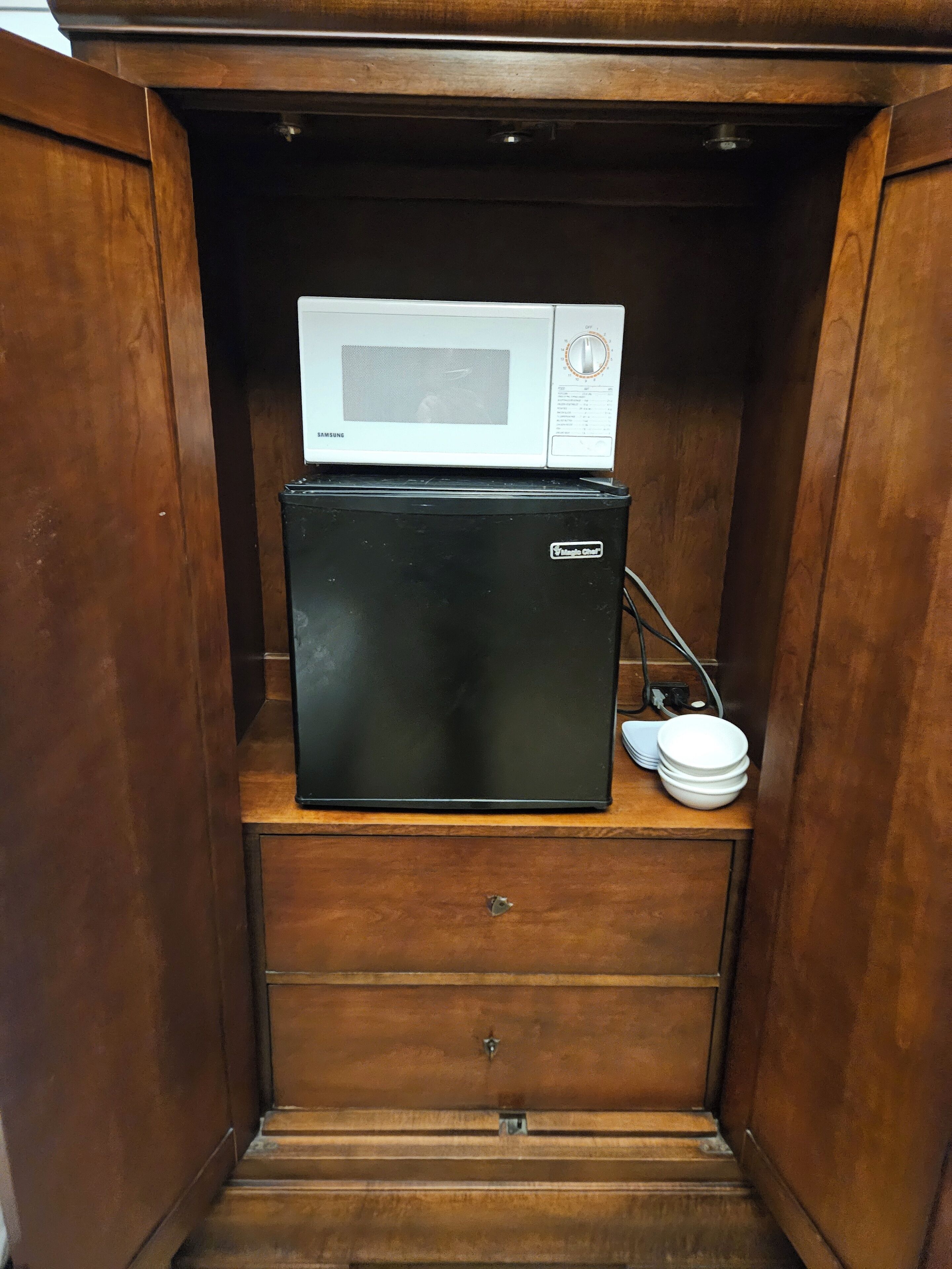 A compact wooden cabinet with a microwave and a black refrigerator inside.