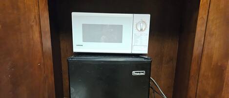 Ein kompakter Holzschrank mit einer Mikrowelle und einem schwarzen Kühlschrank darin.