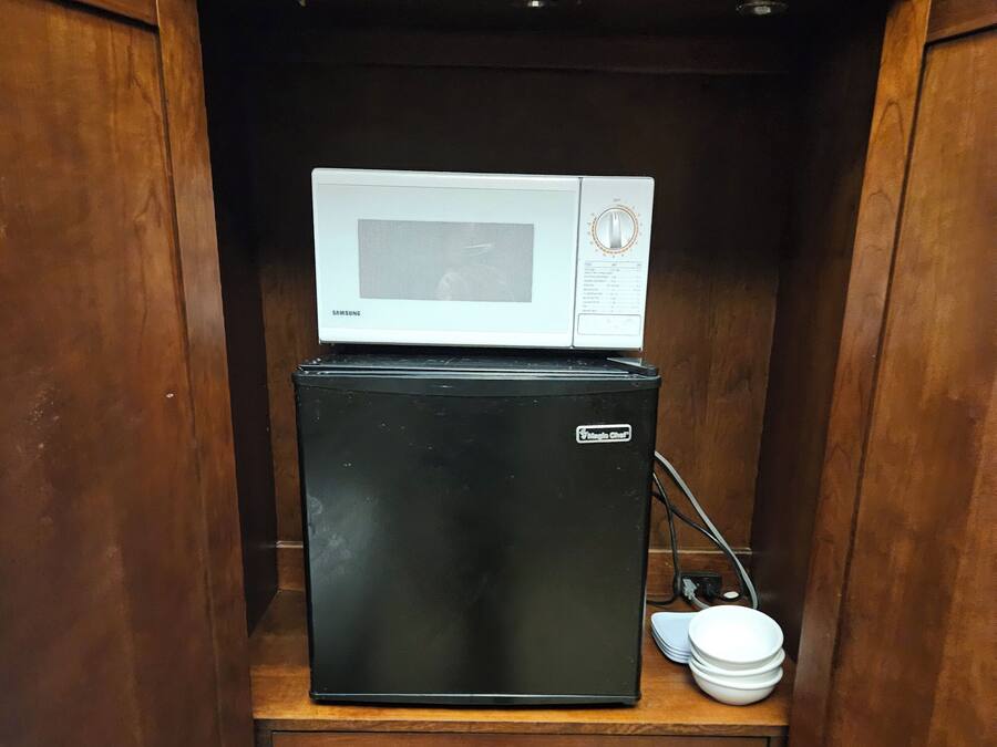 A compact wooden cabinet with a microwave and a black refrigerator inside.