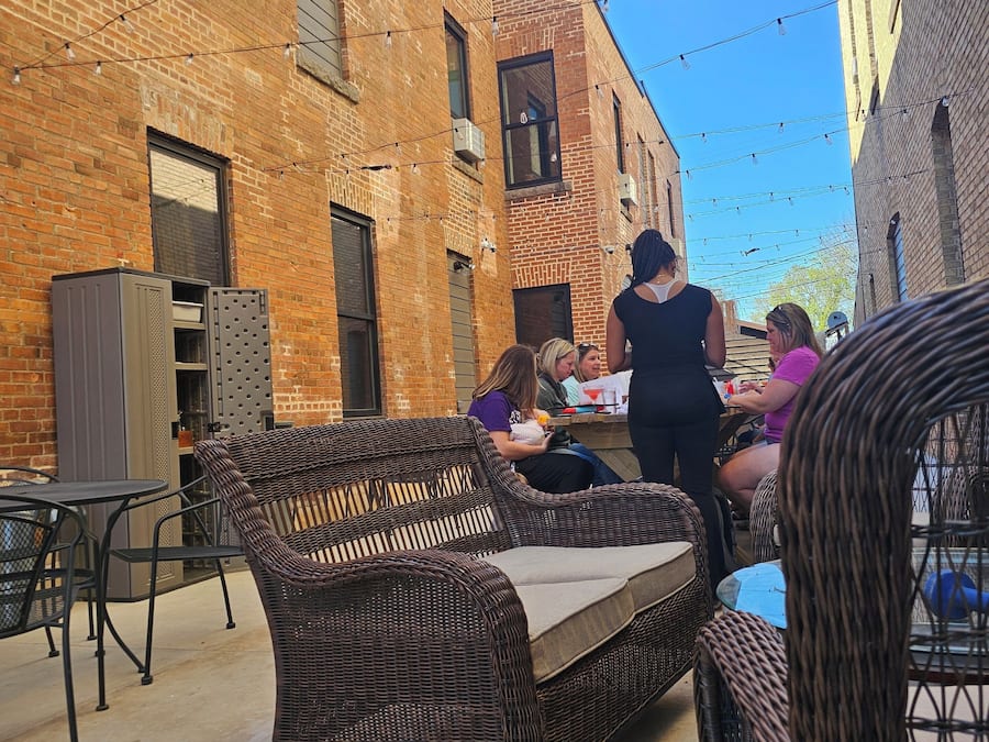An outdoor seating area with wicker furniture, a brick building, and string lights.
