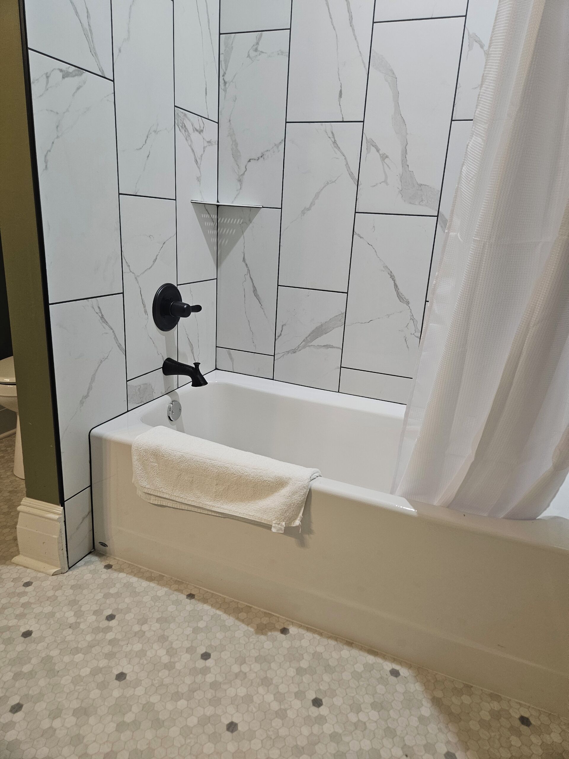Ein Badezimmer mit einer Badewanne, weißen Marmorfliesen, einem Handtuch und einer Duschvorhang.
