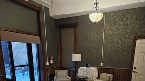 Hotelkamer met groot raam, bureau, stoel, klein tafeltje, lamp en bed.