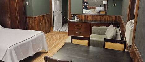 Quarto de hotel com uma cama, uma mesa de jantar de madeira com cadeiras, um sofá, uma televisão na parede e um guarda-roupa de madeira.