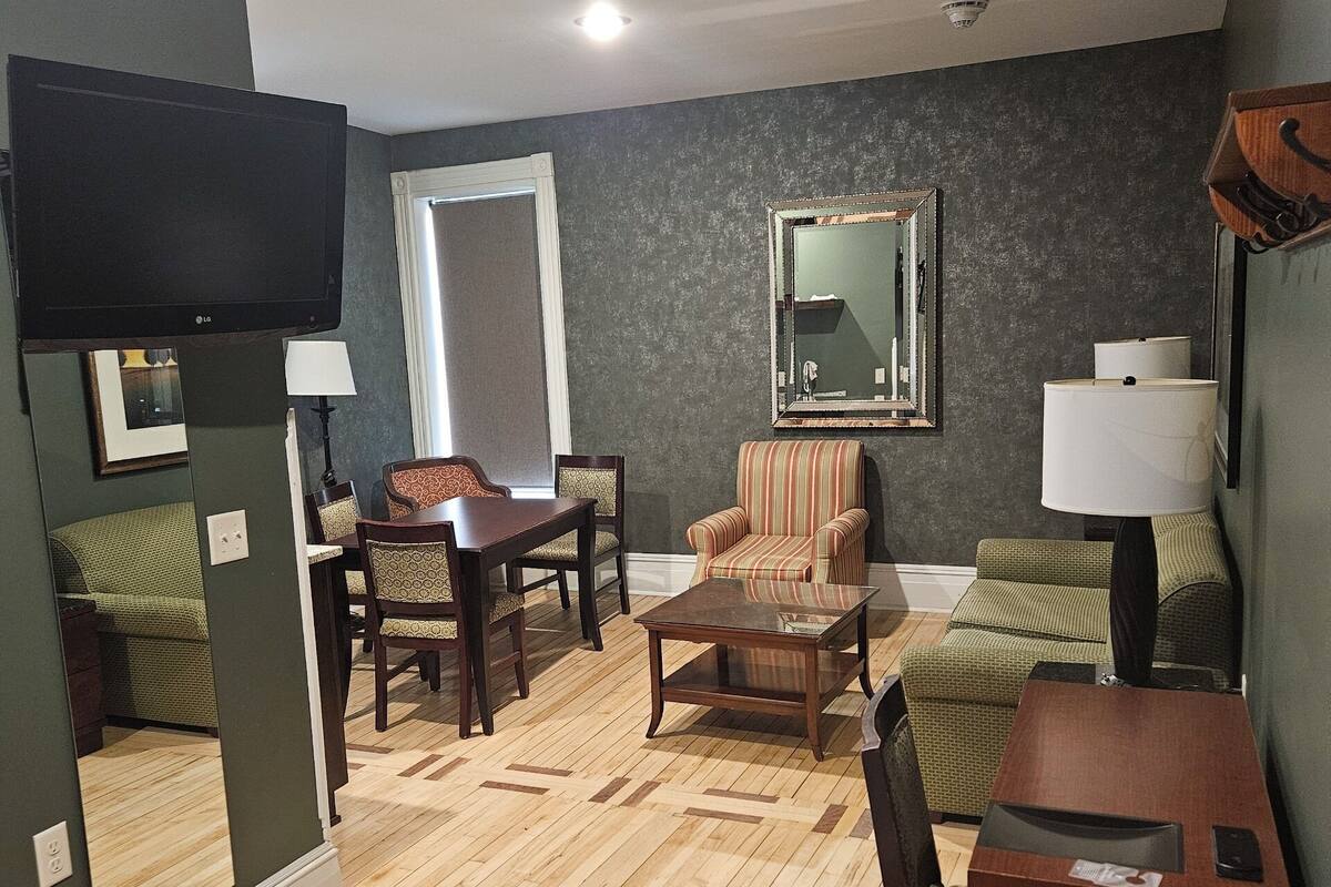Una sala de estar con piso de madera, un televisor montado en la pared, una mesa de comedor con sillas, un sillón a rayas y un sofá.