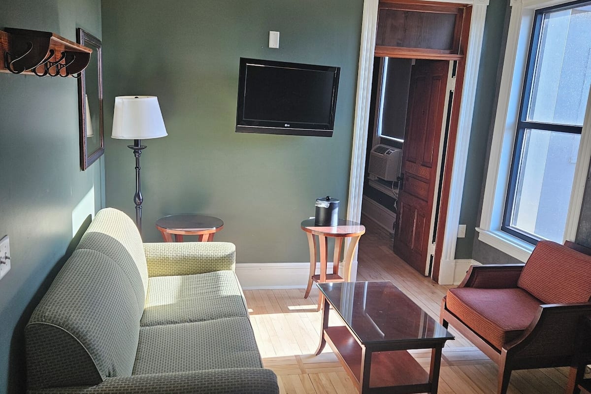 Una sala de estar con una pared verde, un televisor de pantalla plana, un sofá, una silla, una mesita y una lámpara.